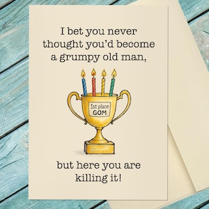 May include: Greeting card with text: "I bet you never thought you'd become a grumpy old man, but here you are killing it!" A gold trophy with "1st place GOM" and four lit candles is in the center. The card is on a cream background.