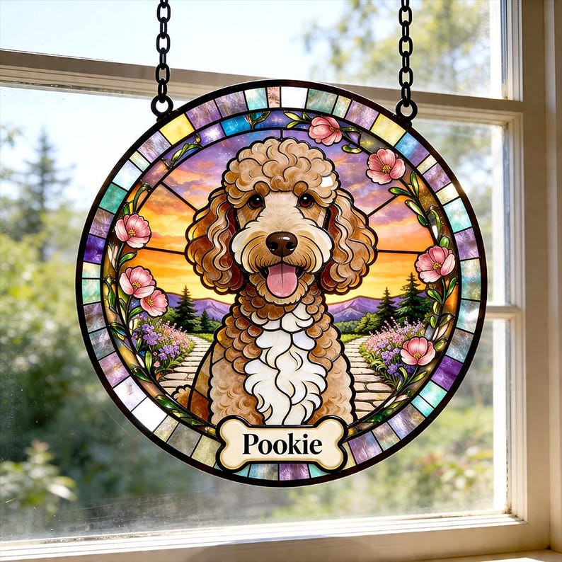 May include: Round stained glass window art featuring a poodle with a happy expression, framed by pink flowers and a colorful border. The dog's name, "Pookie," is on a bone-shaped tag. The artwork hangs from a black chain.