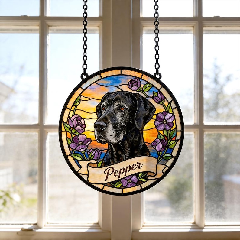 May include: Round stained glass window featuring a black dog portrait with the name "Pepper" on a banner. The design includes purple flowers and a colorful sunset background, suspended by a black chain.