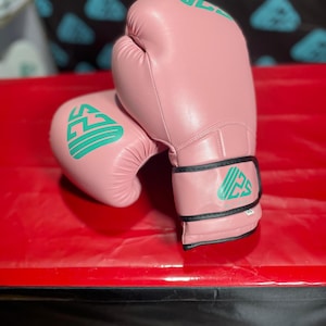 May include: A pair of pink boxing gloves with green lettering that says "WIZZY SPORTS".