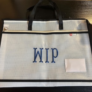 May include: A clear, mesh document bag with black trim and handles. The bag features the embroidered letters "WIP" in blue and a small white label. A zipper runs along the top edge.