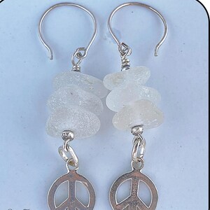 Peut inclure: Boucles d'oreilles argentées avec des breloques en forme de signe de paix. Chaque boucle d'oreille est ornée d'une pile de perles de verre transparentes givrées et d'un crochet argenté. Style bohème.