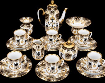 May include: A porcelain tea set featuring a white base with intricate black and gold filigree patterns. The set includes a tall teapot, a creamer, a sugar bowl, a small vase, a bowl, and six cups with matching saucers, all with gold trim.
