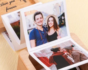 Puede incluir: Una caja de fotos de madera con tapa con bisagras, que muestra varias fotografías impresas. La tapa está grabada con las palabras "Love you forever" y detalles florales. Las fotos muestran parejas en varios entornos.