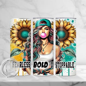 May include: A stainless steel tumbler with a white background and a colorful design. The design features a woman with pink hair, a blue baseball cap, and a pink bubble. The text "FEARLESS BOLD UNSTOPPABLE" is printed on the tumbler.
