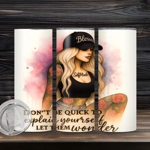 May include: A white tumbler featuring a stylized illustration of a woman wearing a black cap with the word "Blessed" and a black top. The tumbler has the text "DON'T BE QUICK TO explain yourself LET THEM wonder".