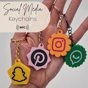 Könnte beinhalten: Vier NFC-fähige Social-Media-Schlüsselanhänger mit den Logos von Snapchat, Pinterest, Instagram und WhatsApp. Die Anhänger sind gelb, rosa, orange und grün, haben verschiedene geometrische Formen und Metallringe zur Befestigung an Schlüsseln.