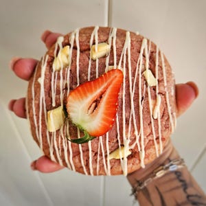 Puede incluir: Una galleta rosa y blanca con chispas de chocolate blanco y una rodaja de fresa en la parte superior.