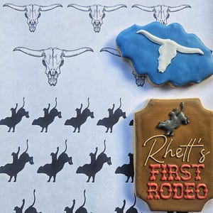 Puede incluir: Una galleta marr&oacute;n y beige decorada con el texto "Rhett's First Rodeo" en glaseado rojo y blanco. La galleta est&aacute; rodeada de un fondo blanco con un patr&oacute;n de cr&aacute;neos de toro negros y siluetas de vaqueros montando toros.