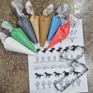 Puede incluir: Un conjunto de ocho mangas pasteleras llenas de glaseado de diferentes colores, junto con una hoja de papel con plantillas de decoraci&oacute;n de galletas con tem&aacute;tica de vaquero. Las plantillas incluyen im&aacute;genes de botas de vaquero, sombreros, caballos, cactus y un vaquero montando a caballo.