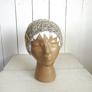 May include: A brown and white knit beanie with a white paper crown on a brown paper mannequin head.