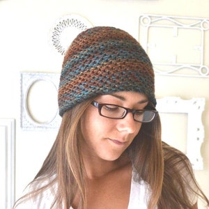 Peut inclure: Une femme portant un bonnet en tricot brun, bleu et vert avec un motif rayé brun et noir. Elle porte également des lunettes.