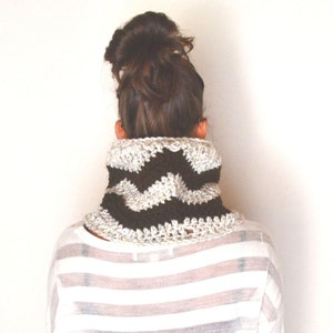 May include: A brown and white chevron patterned crocheted neck warmer. The neck warmer is worn by a person with brown hair pulled back in a bun.