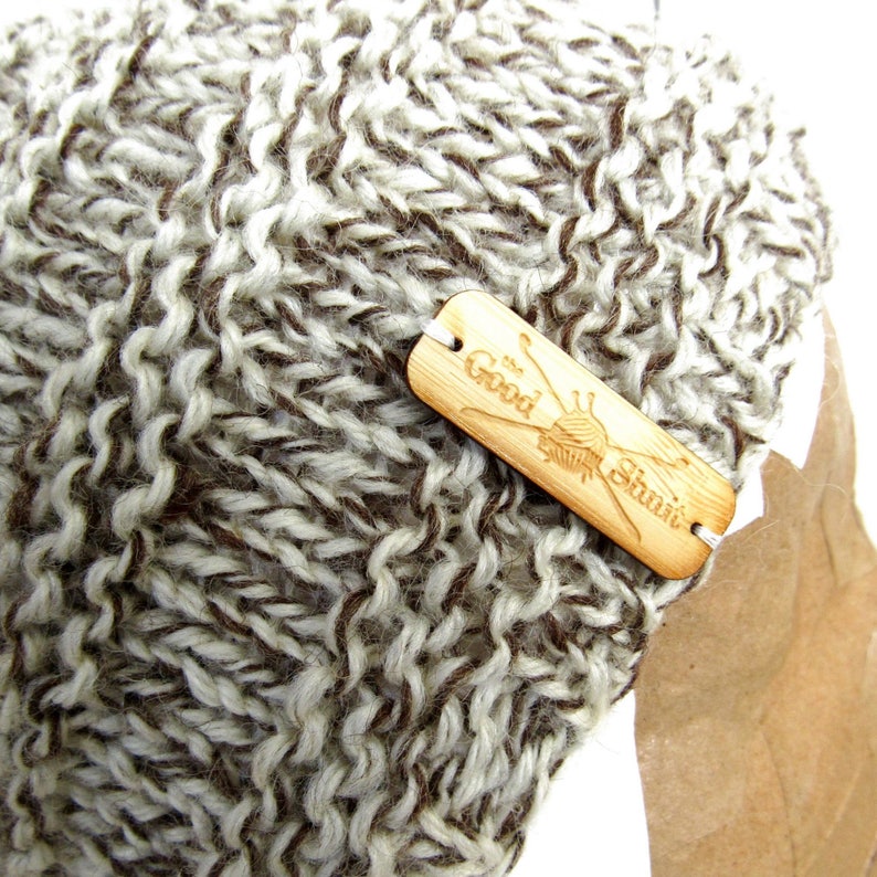 May include: A brown and white knitted beanie with a wooden tag that says "The Good Stitch".