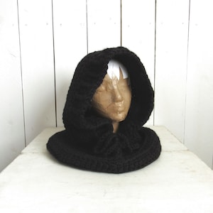 May include: Black crocheted hooded cowl with a wide, gathered neckline. The cowl is made of a soft, chunky yarn and is perfect for keeping warm in the winter.