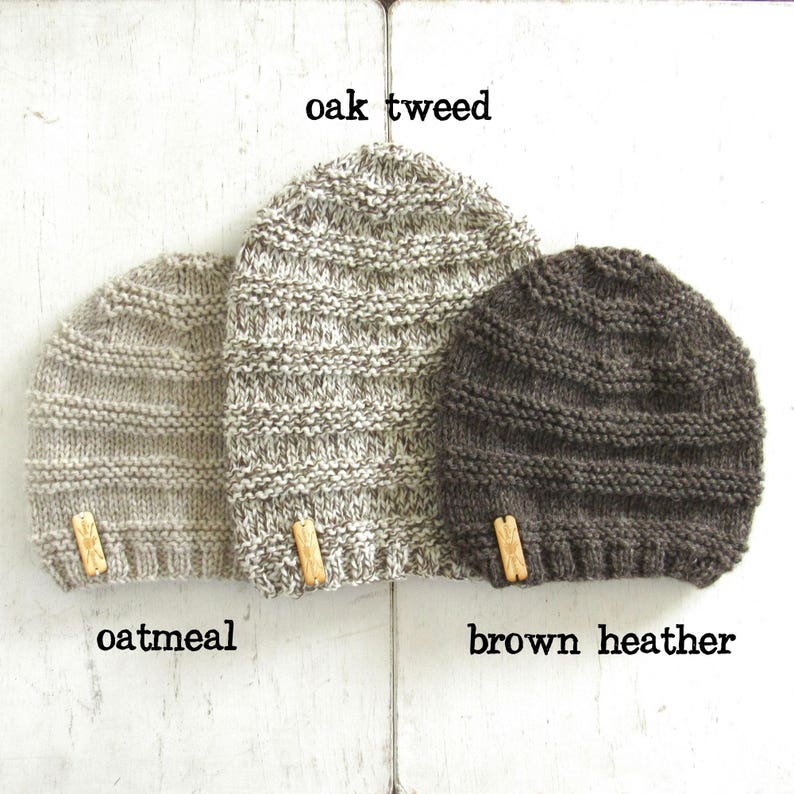 May include: Three knitted beanies in different colors: oatmeal, oak tweed, and brown heather. Each beanie has a small wooden tag attached.