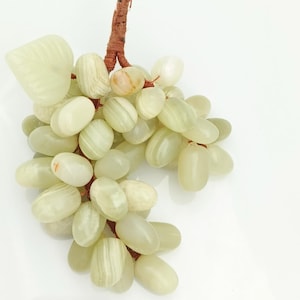 Może przedstawiać: Gronia zielonych winogron rzeźbionych z jadeitu, z brązowym pędem. Winogrona są ułożone w gronie i mają gładkie, polerowane wykończenie.