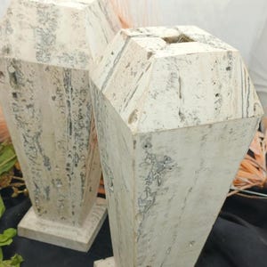 May include: Two white ceramic vases with a geometric design. The vases have a textured surface and a square base.