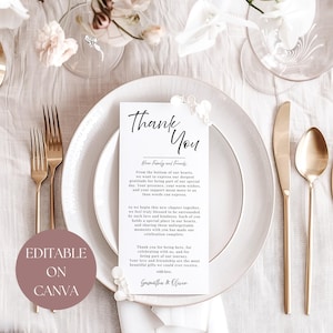以下が含まれることがあります： 白いお皿、金色のカトラリー、そして「Thank You」カードが置かれた結婚式のテーブルセッティング。カードにはエレガントな筆記体と心からのメッセージが書かれています。「Editable on Canva」の文字も表示されています。