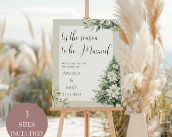 May include: A wedding sign on a wooden easel. The sign reads "Tis the season to be Married" with the names Angela & Mike and the date 26-12-2025. The sign has a floral and Christmas tree design. A round sticker says "3 Sizes Included".