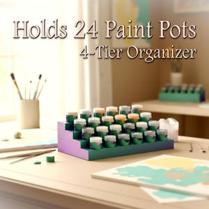 May include: A 4-tier paint pot organizer in green and purple holds 24 paint pots. The organizer is on a table with paintbrushes and a painting in progress. Text on the image reads: Holds 24 Paint Pots, 4-Tier Organizer.