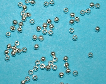 Könnte beinhalten: Eine Streuung von silberfarbenen Metallperlen auf blauem Hintergrund. Die Perlen sind rund und haben ein kleines Loch in der Mitte.
