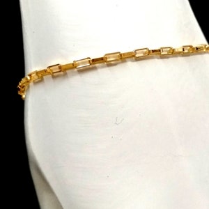 Puede incluir: Un brazalete de cadena de oro con un diseño de cadena de caja. La cadena está hecha de pequeños eslabones rectangulares.
