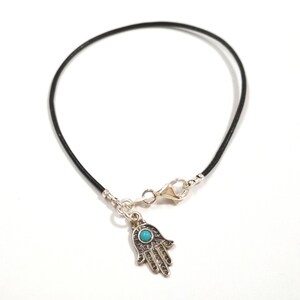 May include: A black leather bracelet with a silver hamsa charm featuring a turquoise blue stone in the center.