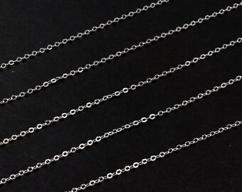 May include: Four silver chains laid out in parallel lines on a black background. The chains are made of small, linked oval shapes.