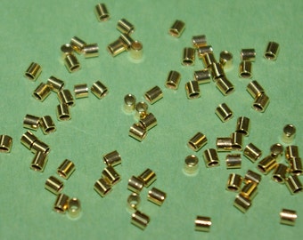 May include: A large quantity of gold-colored metal jump rings. The jump rings are small and round, and they are scattered on a green surface.