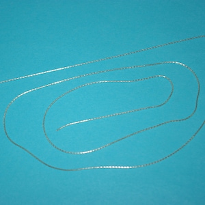 May include: A silver chain necklace on a blue background. The chain is made of small, linked squares.