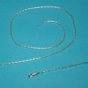 May include: A silver chain necklace with a lobster clasp closure. The chain is made of small, linked, oval-shaped pieces.
