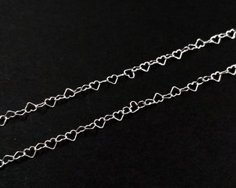 以下が含まれることがあります： 黒い背景に、銀色のハート型のチェーンが2本。チェーンは、小さなハート型のリンクが互いにつながってできています。