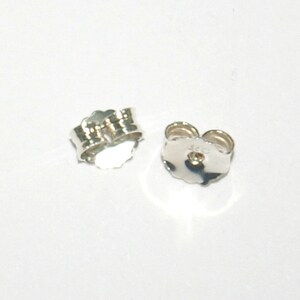 Puede incluir: Dos respaldos de pendientes de plata, uno con una marca visible de "925".
