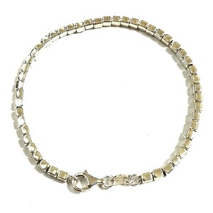 Puede incluir: Un brazalete de plata con una cadena de eslabones cuadrados y un cierre de langosta.