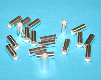 Può includere: Una collezione di perline a crimpare in metallo color argento, sparse su una superficie blu. Queste perline sono utilizzate per la creazione di gioielli e l'artigianato.