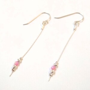 May include: A pair of silver dangle earrings with a pink and white bead design.