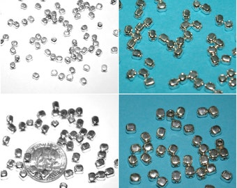Könnte beinhalten: Nahaufnahme von silbernen Metallperlen, einige sind auf einer weißen Oberfläche verstreut, andere auf einer blauen Oberfläche. Die Perlen sind quadratisch mit abgerundeten Kanten.