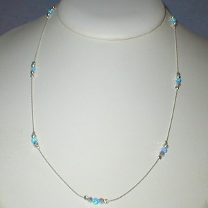 May include: A silver chain necklace with light blue opal beads. The necklace is displayed on a white mannequin bust.