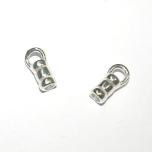 Peut inclure: Deux embouts métalliques argentés pour la fabrication de bijoux. Chaque embout a une petite boucle en haut et un corps cylindrique.