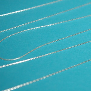 May include: Three silver chains on a blue background. The chains are made of small, linked squares.