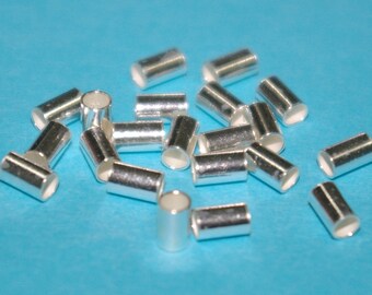 Può includere: Un gruppo di perline a crimpare in metallo color argento, sparse su una superficie blu.