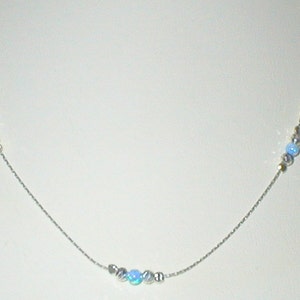 May include: A silver chain necklace with light blue opal beads. The necklace has three clusters of beads, two on the top and one in the center.