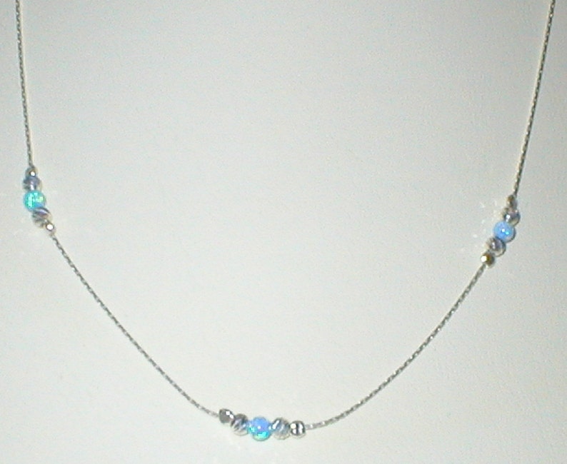 May include: A silver chain necklace with light blue opal beads. The necklace has three clusters of beads, two on the top and one in the center.
