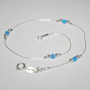 Könnte beinhalten: Ein silbernes Fußkettchen mit einer zarten Kette und blauen Opalperlen. Das Fußkettchen hat einen Karabinerverschluss.