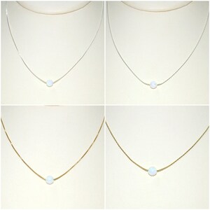 May include: Four necklaces with a single, round, white opal pendant. Two necklaces have silver chains, and two have gold chains. The pendants are centered on the chains, and the background is a light beige.