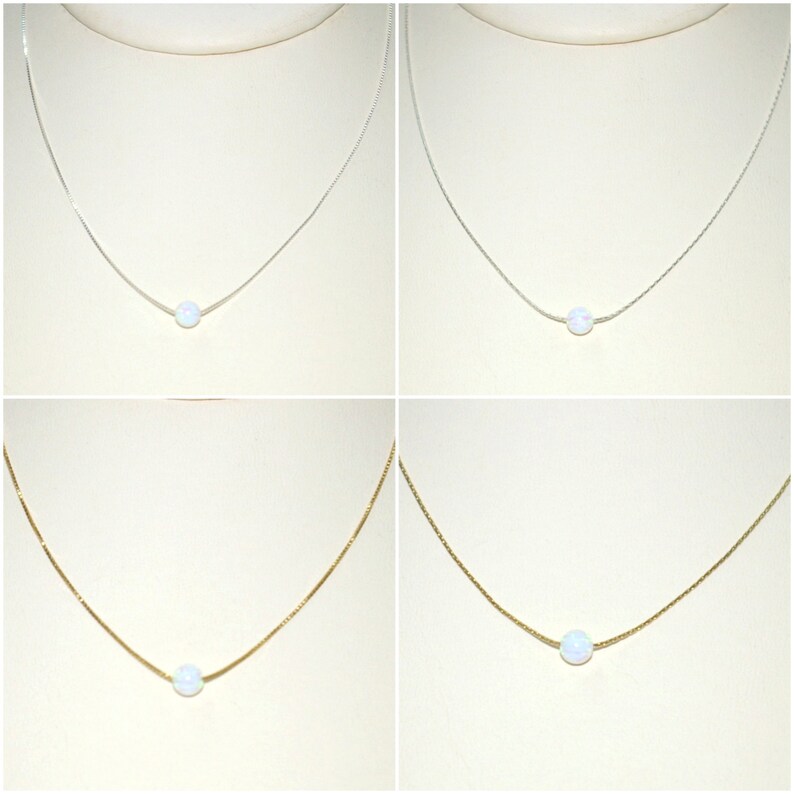 May include: Four necklaces with a single, round, white opal pendant. Two necklaces have silver chains, and two have gold chains. The pendants are centered on the chains, and the background is a light beige.