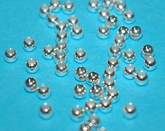Könnte beinhalten: Eine große Menge silberfarbener Metallperlen, verstreut auf einer leuchtend blauen Oberfläche. Die Perlen sind rund und haben einen leicht erhöhten Rand.