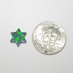 May include: A green and blue iridescent opal cabochon cut in the shape of a six-pointed star. The opal is approximately the size of a US dime.