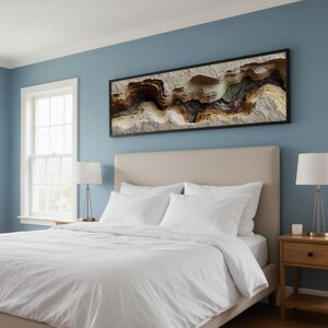 May include: A bedroom with a light blue wall, a bed with white bedding, and a framed abstract art piece. Two windows are on the left side of the bed. A nightstand with a lamp is on the right side of the bed.